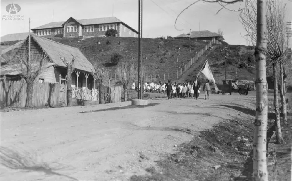 Alumnado de la Escuela 16 desfila por las calles céntricas con una gran bandera al frente, alrededor de 1932. Colección Capraro en Archivo Visual Patagónico.