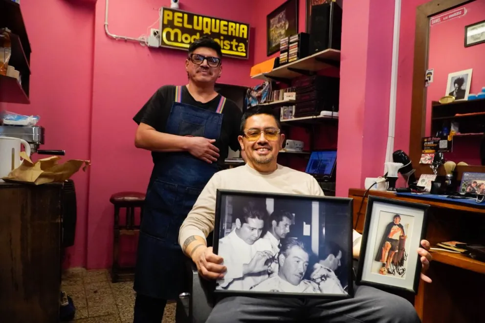 Daniel (parado) y "Cito" sentado, muestran dos símbolos de su salón, sus formadores en el oficio y el cuadrito de "El Príncipe" Francescoli. Fotos: Facundo Pardo